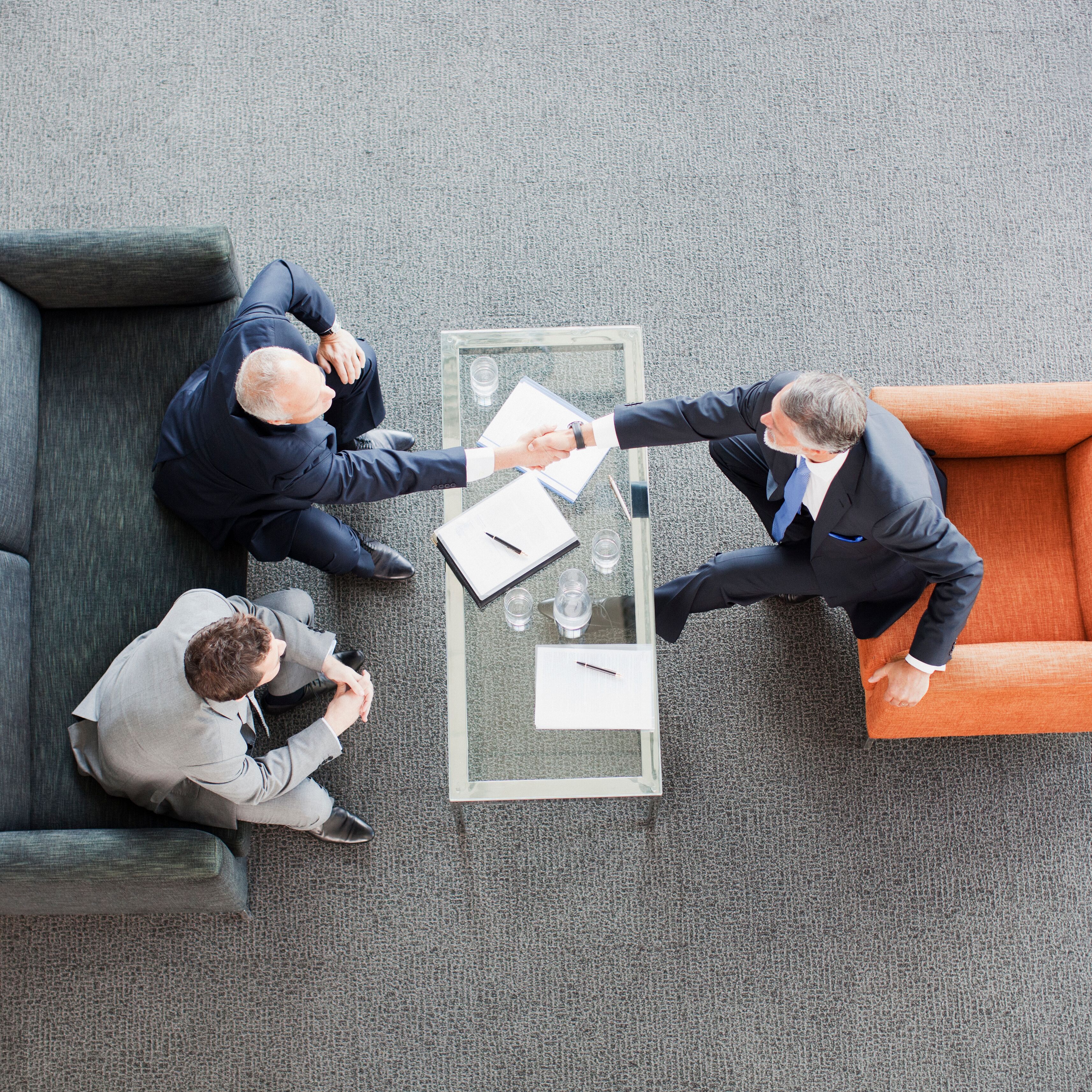 Businessmen shaking hands across coffee table in office lobby